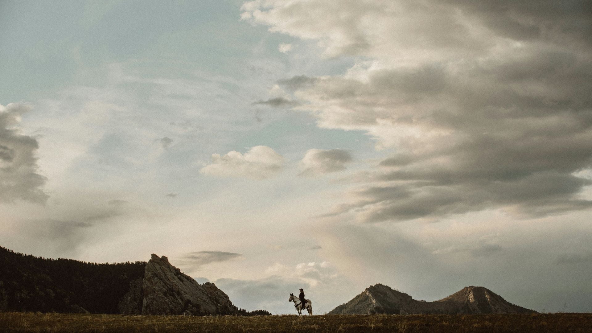 a person on a horse in the distance with mountains and sky background