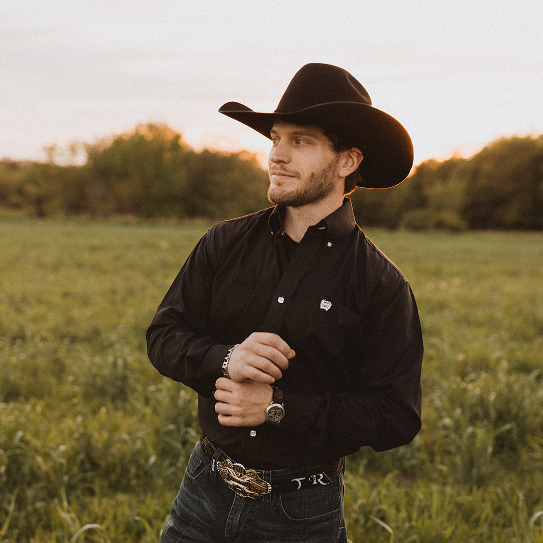 a man looking into the distance in a black shirt and cowboy hat 