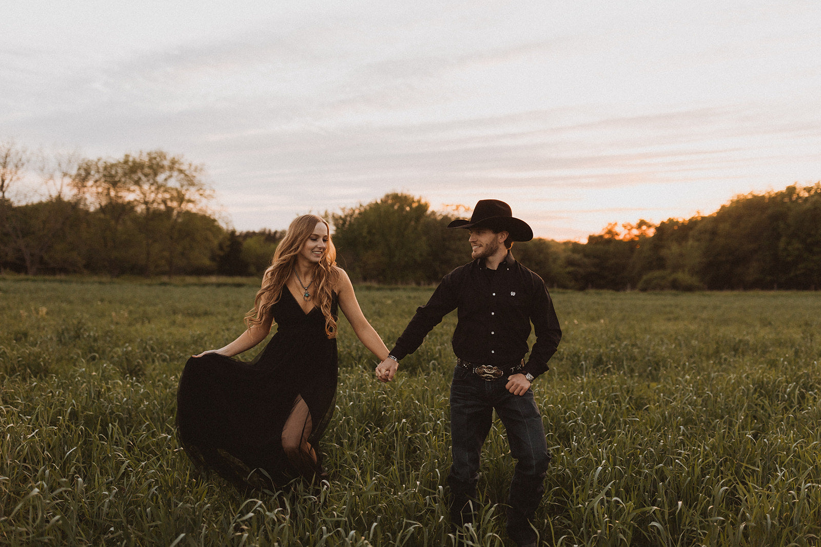 a couple both wearing black holding hands walking in a field